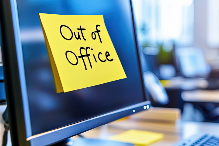 yellow sticky note with "out of office" written placed on computer monitor